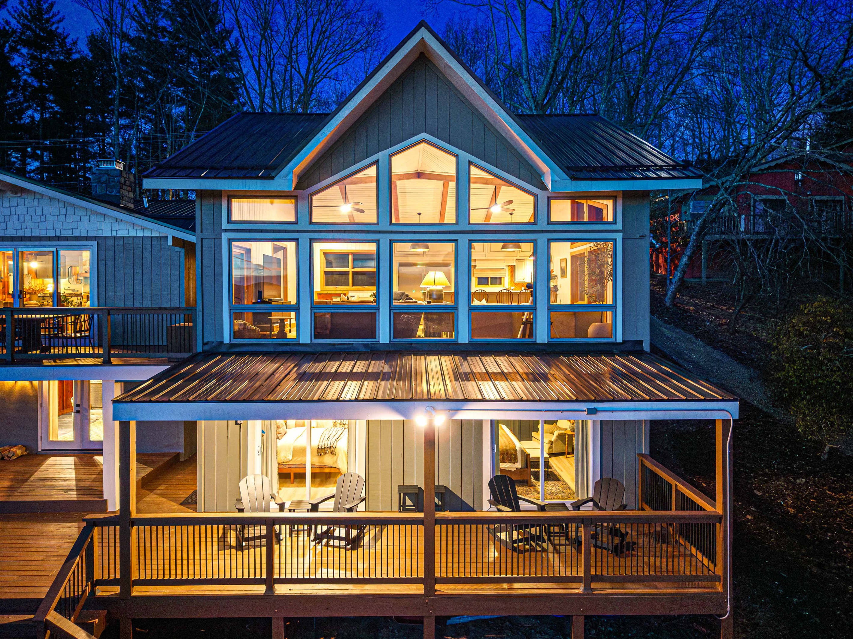 Evening exterior view of the home showcases the new side of the house glowing warmly against the mountain backdrop, with multiple deck levels designed for outdoor living.