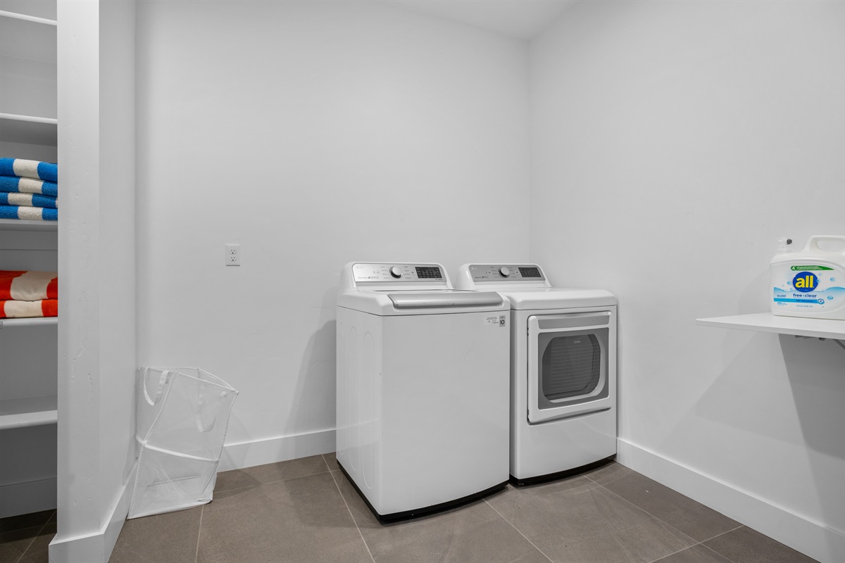 Full-size washer and dryer in a spacious laundry room with shelving.