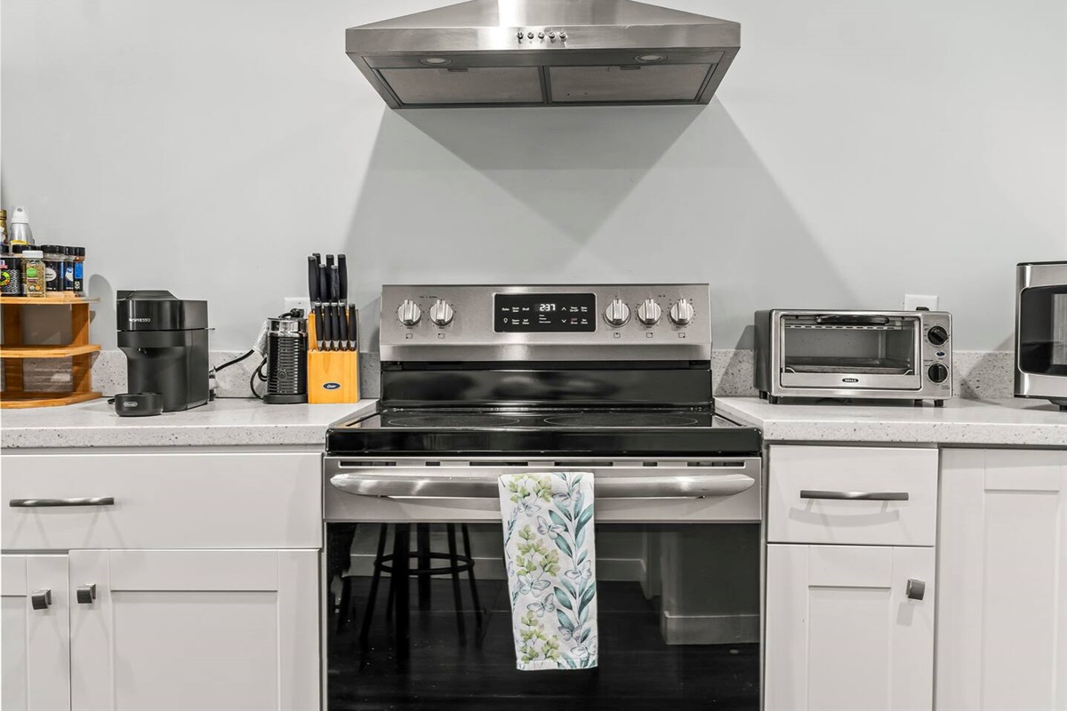Modern cooking area featuring a full electric stove, stainless vent hood, knife set, and essential cookware.