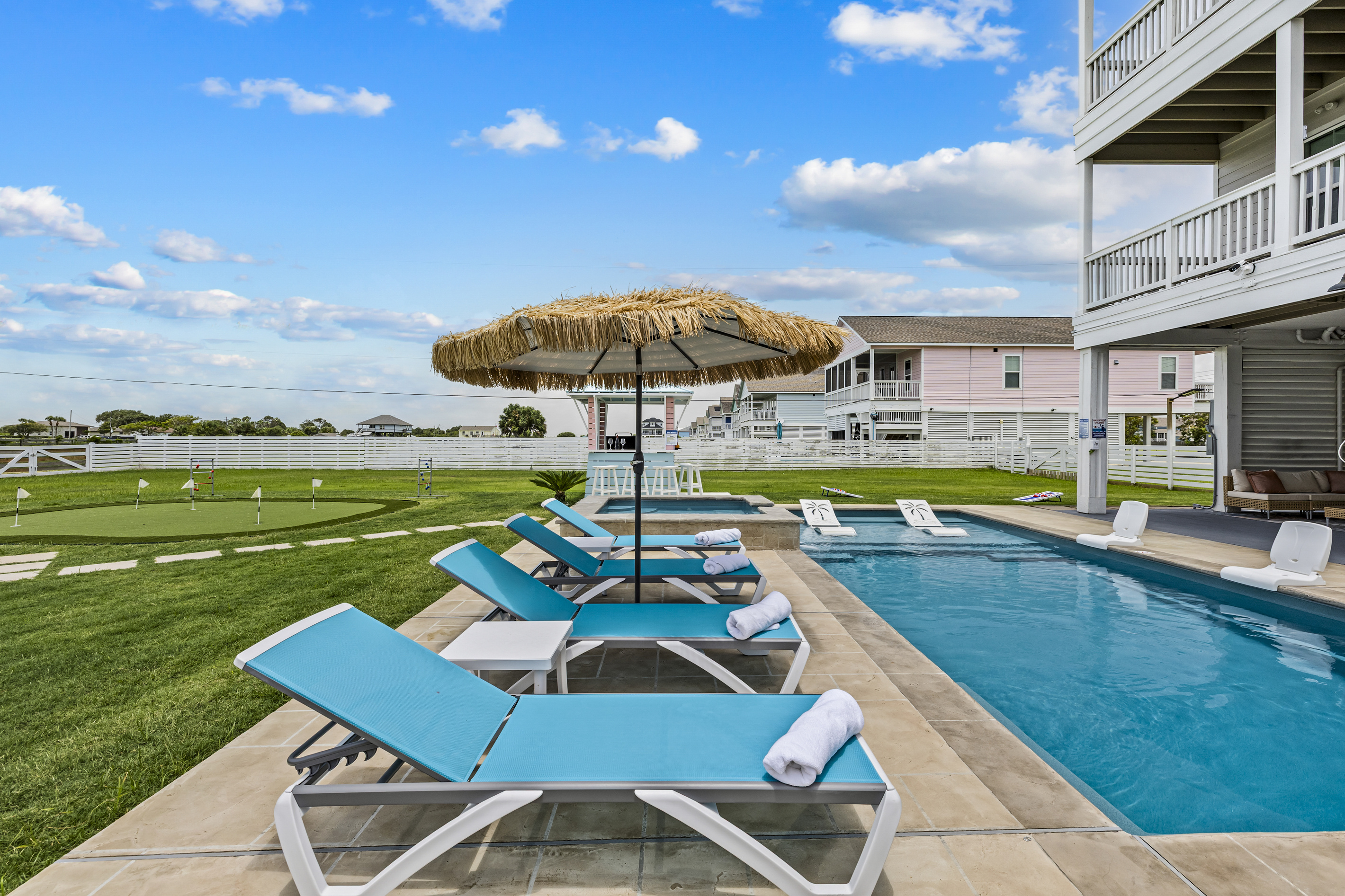 "Step into private backyard oasis featuring a sparkling pool and hot spa surrounded by modern walkways, mini golf, fire pit, and resort style vibes perfect for relaxing after a day at the beach".