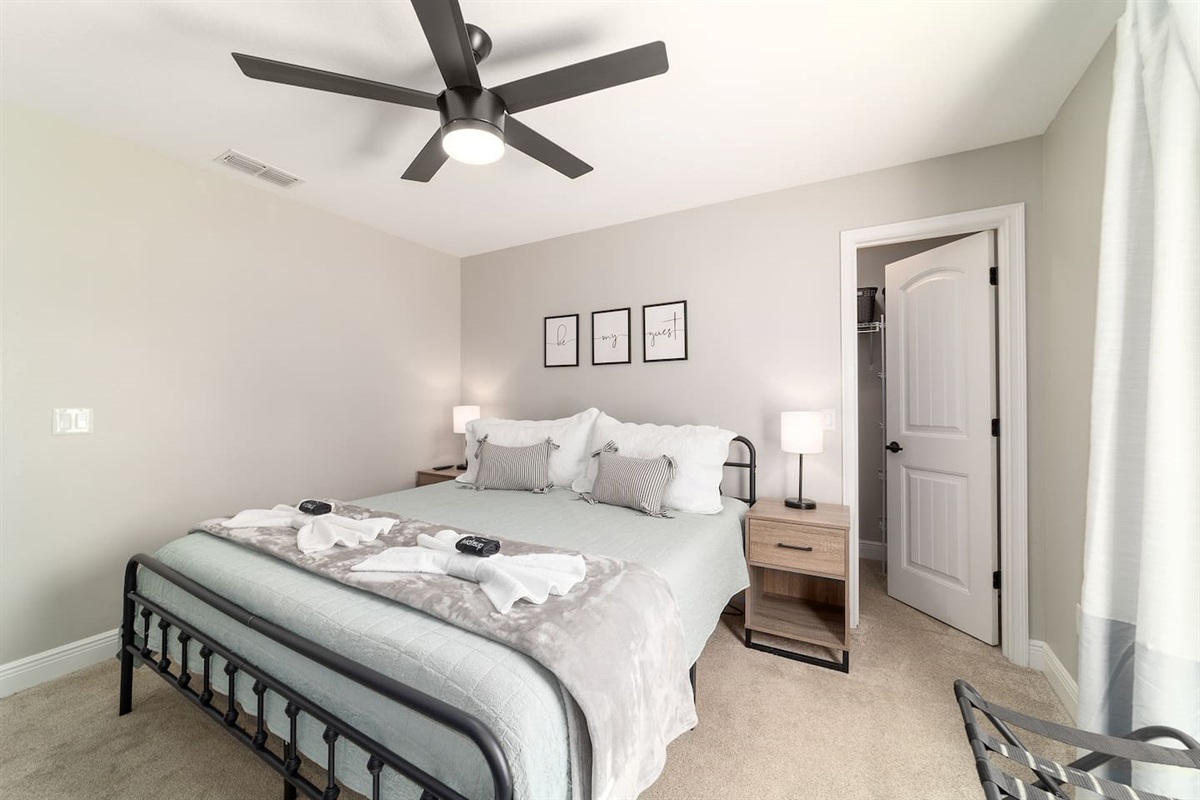 Rest well in this warm, thoughtfully styled king bedroom featuring a sleek metal frame bed, soft neutral tones, and cozy bedding. With ample natural light and welcoming décor, this room offers the perfect blend of comfort and modern charm.