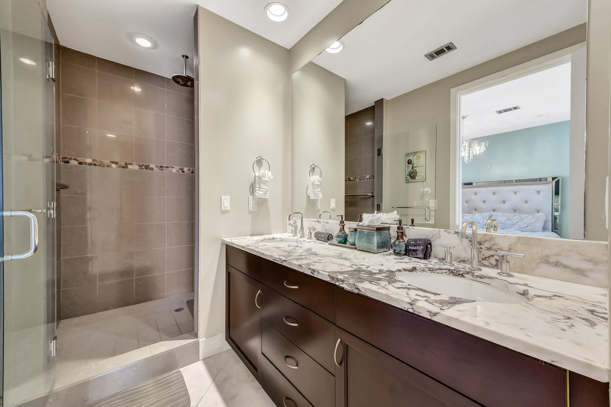 Master bathroom with double-sinks and walk-in rain shower.  The rain shower has a handrail and a portable shower chair.  