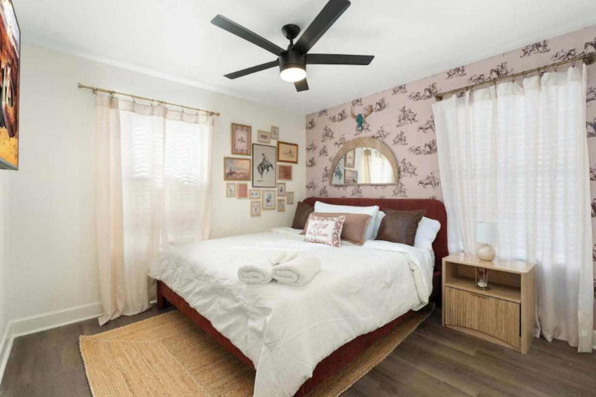 Cozy guest bedroom with burgundy headboard, patterned wallpaper, and natural light—intimate and inviting with vintage charm.