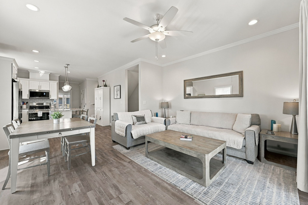 Open-concept main living layout showcasing seamless flow between the coastal dining area, comfortable living room, and modern kitchen beyond.   