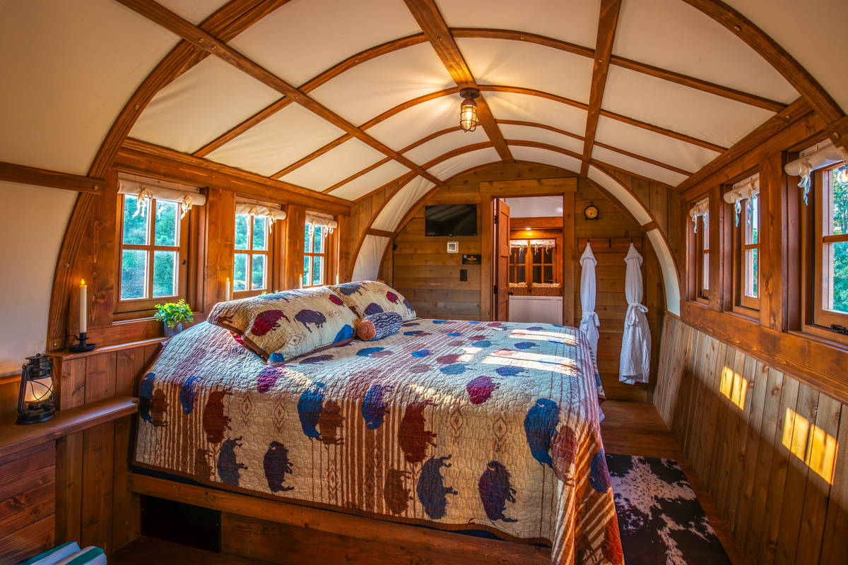 Cozy king bed tucked inside the covered wagon with warm wood finishes and a private bathroom.