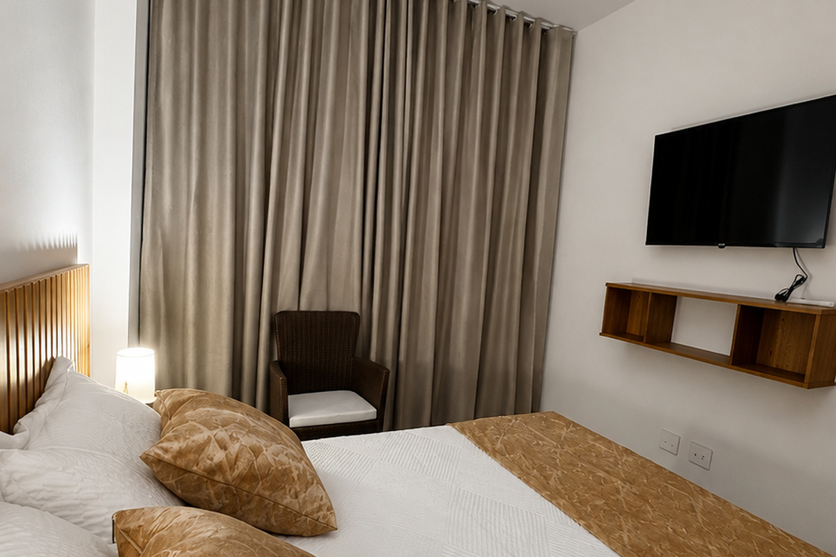 Dormitorio con TV montada en la pared, aire acondicionado tipo split, iluminación junto a la cama y estantería de almacenamiento, ofreciendo comodidad práctica durante toda la estancia.