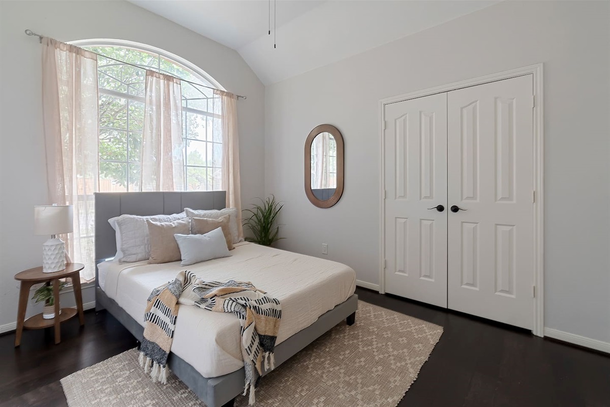Inviting bedroom featuring two cozy double beds, adorned with plush pillows. A stylish wall mirror adds a touch of decor, complemented by a spacious closet for organization. Natural light streams through the window creating a tranquil atmosphere.