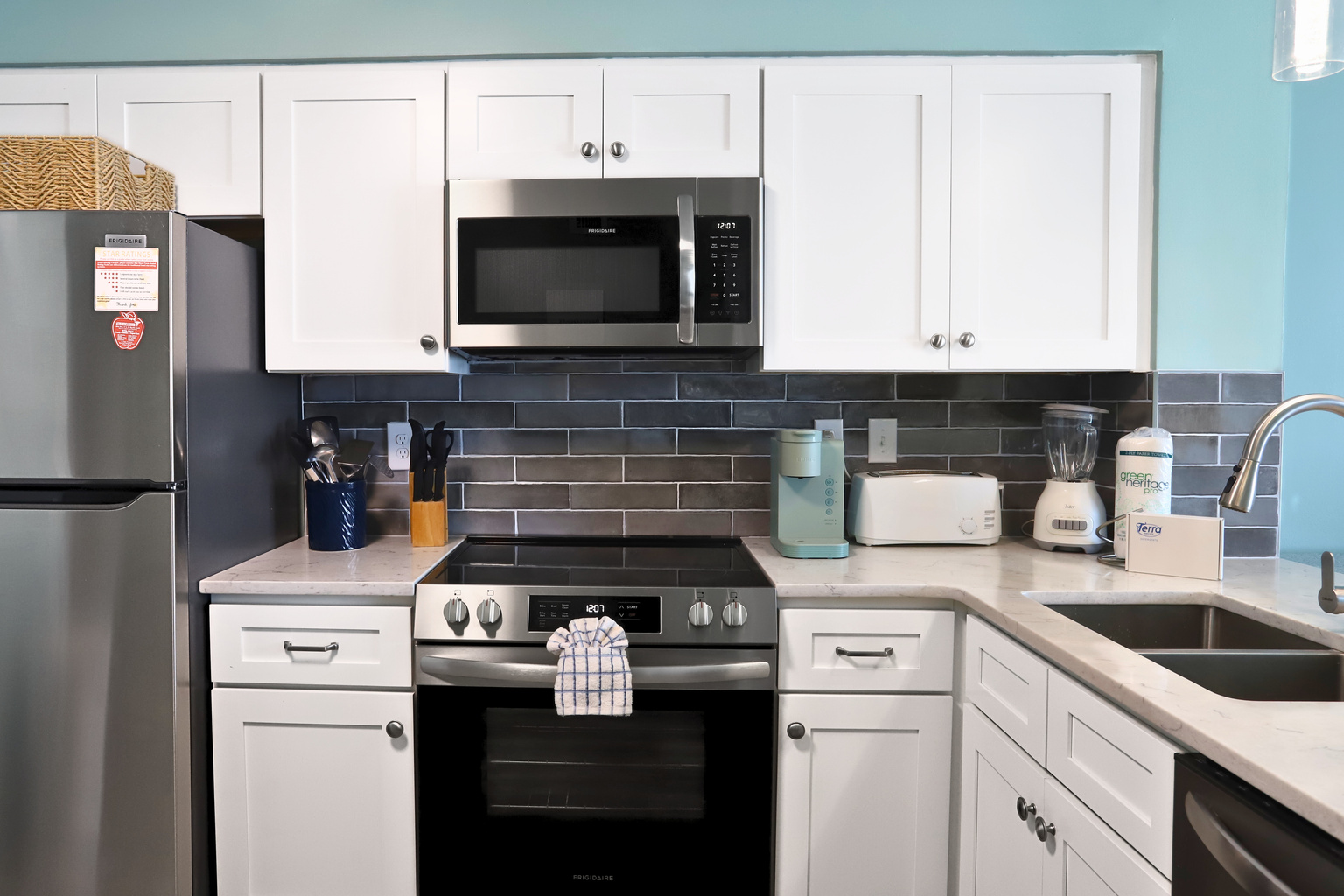 A modern kitchen featuring a sleek silver fridge, countertop stove with oven,dishwasher, microwave, and state-of-the-art appliances—fully equipped with everything you need for effortless cooking and dining.