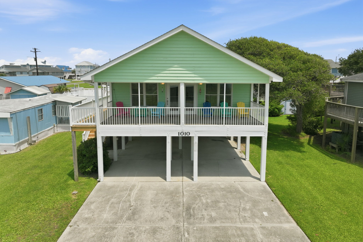 Aerial view showcasing the home's spacious wraparound porch, covered parking, and coastal setting