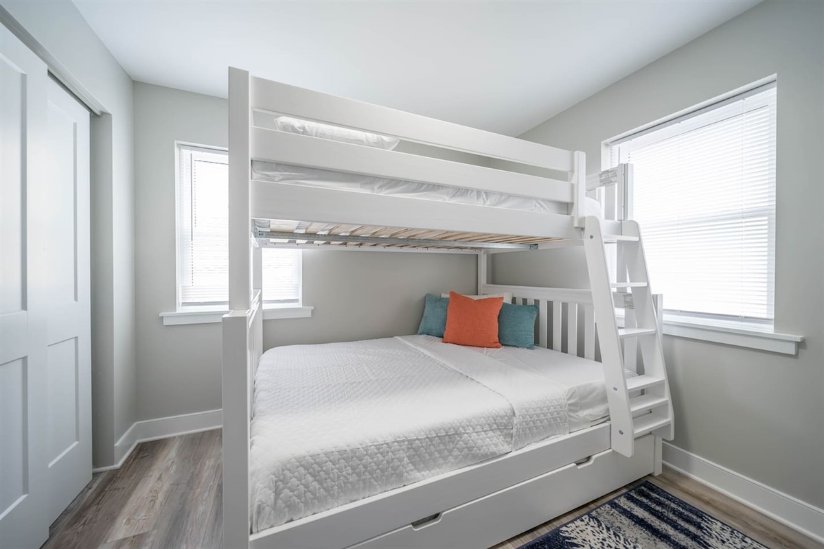 Bright bunk bedroom with sturdy white bunks, crisp linens, and natural light from two windows. Designed for comfort and practicality, this space is ideal for kids or friends to rest, recharge, and enjoy a relaxed stay together.
