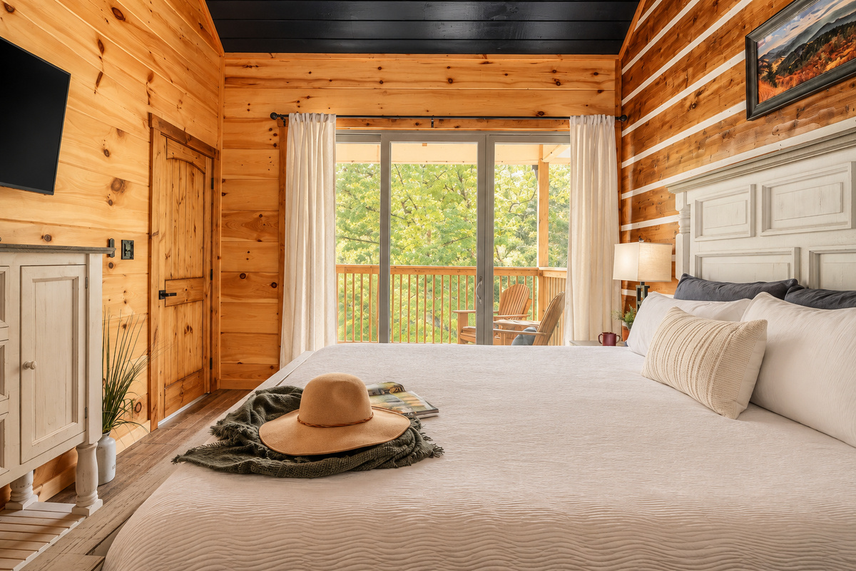 King bed, TV, dresser, and glass doors to a private deck with Adirondack chairs.