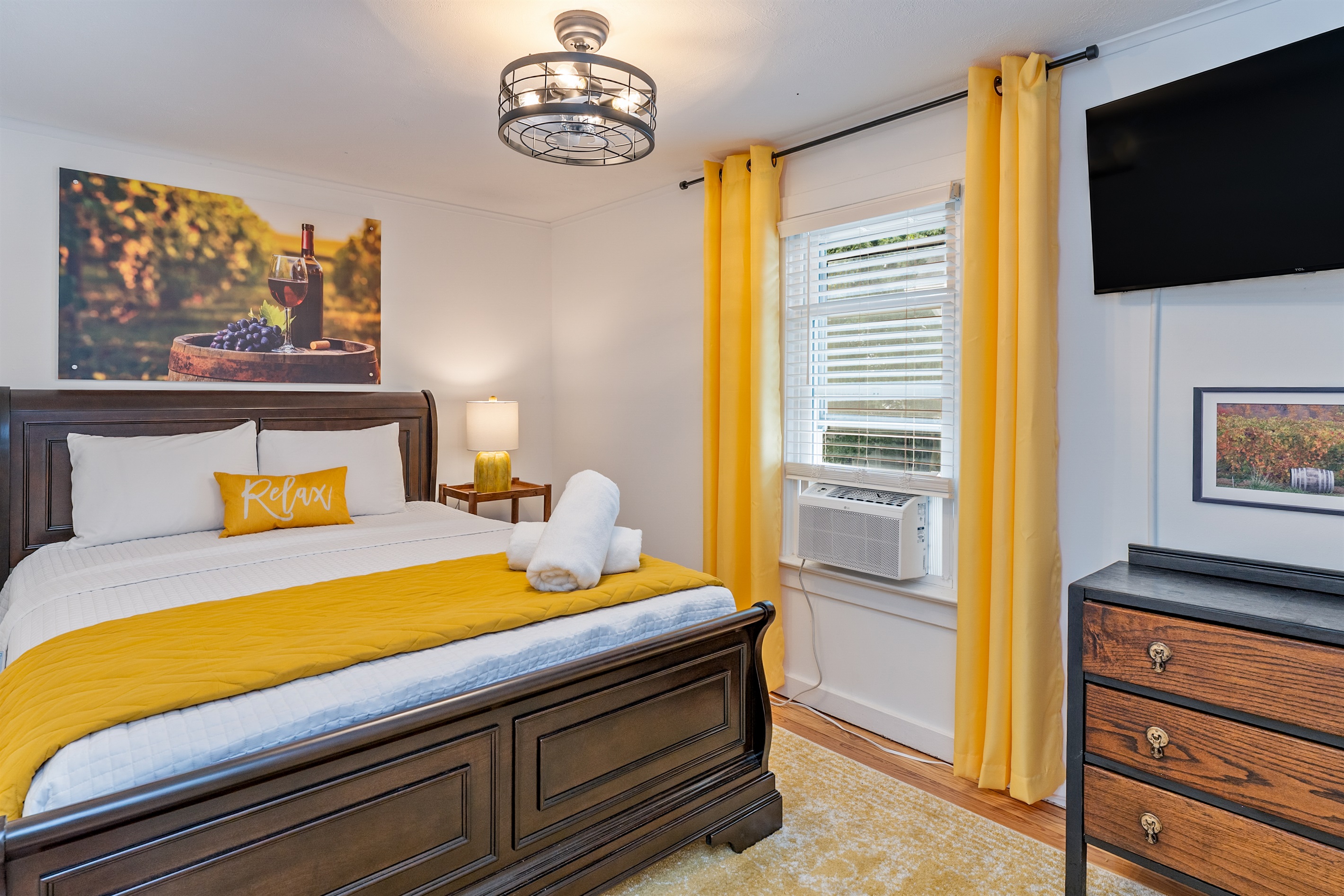 Bright and inviting, this vineyard-themed queen room features a plush bed, vibrant yellow accents, and a flat-screen TV—ideal for relaxing after a day of wine tasting. Bedroom #2