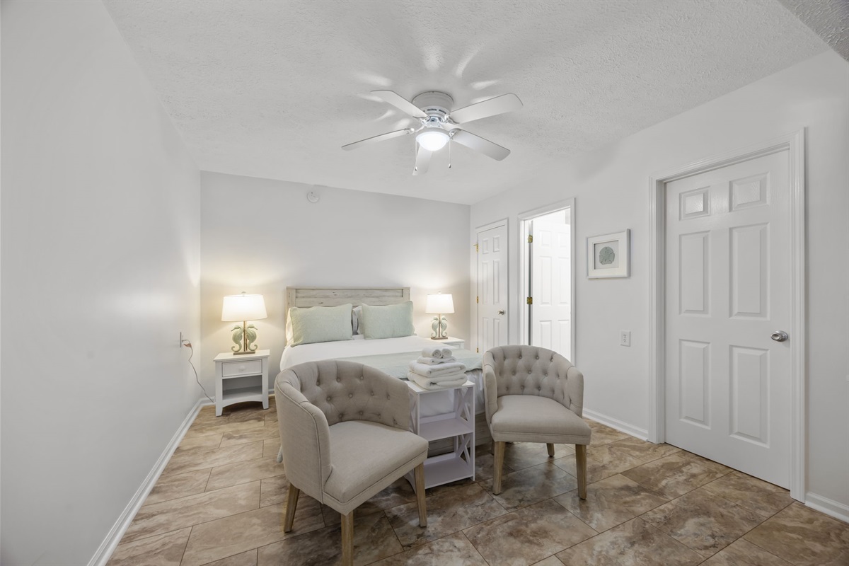 Spacious ground-level bedroom with TV, seating area, and sliding doors leading to the entry sitting area