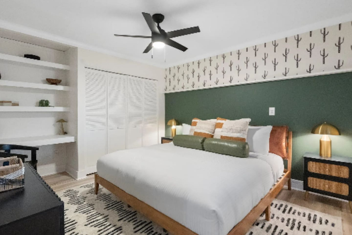 A deep green accent wall and hand-illustrated cactus print set a moody, grounded tone, while the built-in shelving and desk nook add a quiet workspace for anyone who needs one. Brass lamps warm up the whole corner.