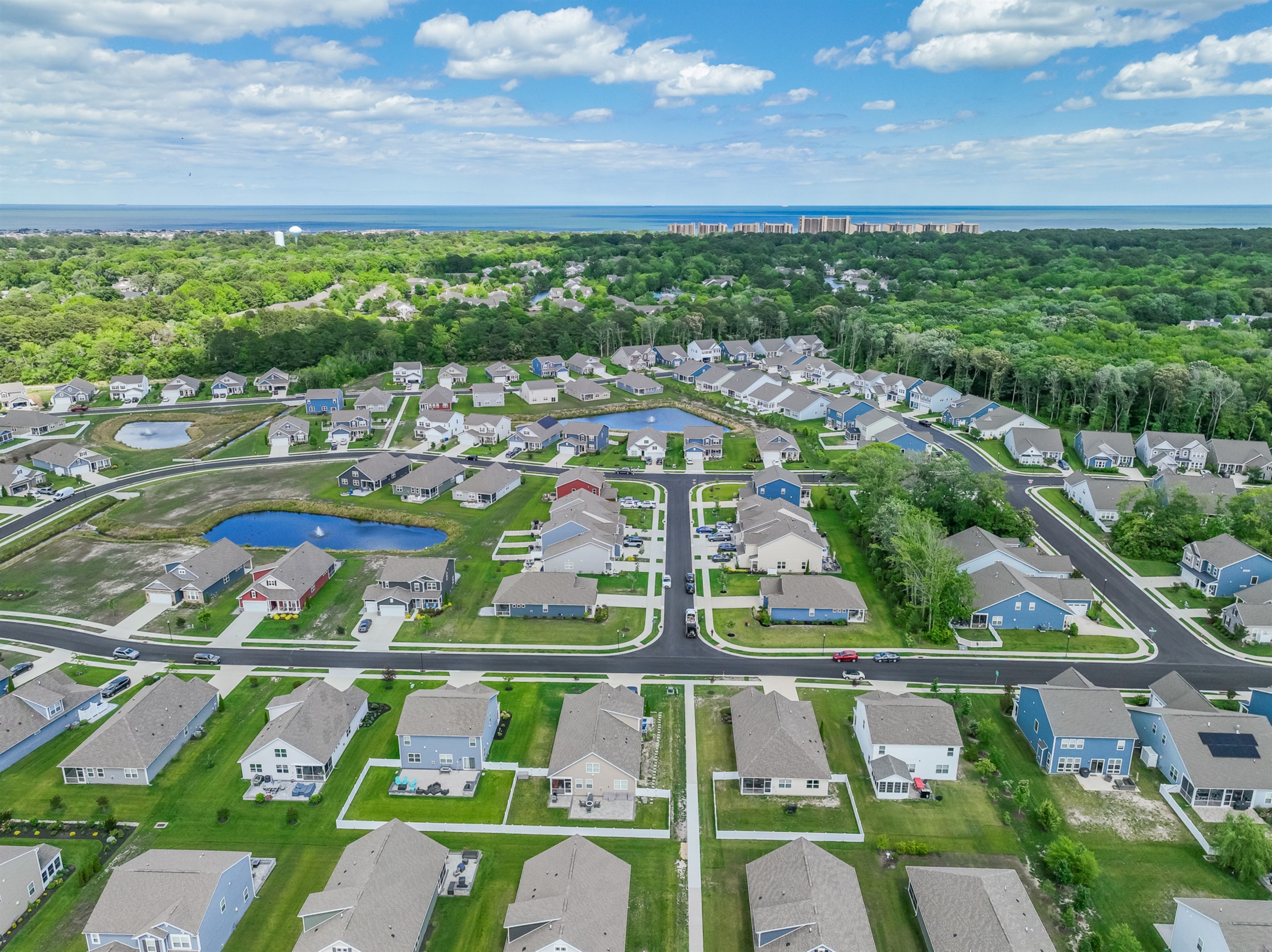 Aerial view of Ocean View Beach Club North: tranquil community ponds, tree-lined streets, and coastal greenery, with the Atlantic horizon in the distance.