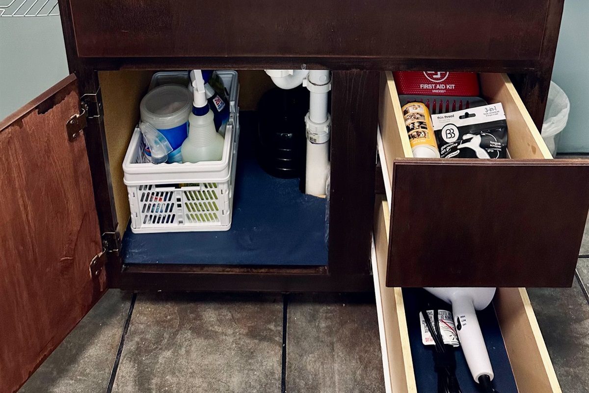 Basement bathroom cabinet stocked with bathroom-specific cleaning products and drawers including a lint roller, first aid kit, hair dryer, and toothbrushes/toothpaste (stored inside). Stocked so guests using the lower level have everything they need.