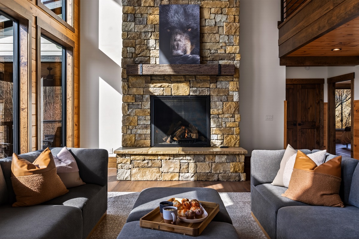 Gather beneath 30-foot vaulted ceilings surrounded by a wall of windows. Relax on the large sectional sofa beside the luxury fireplace with stunning floor-to-ceiling stone, creating a warm and unforgettable mountain lodge atmosphere.