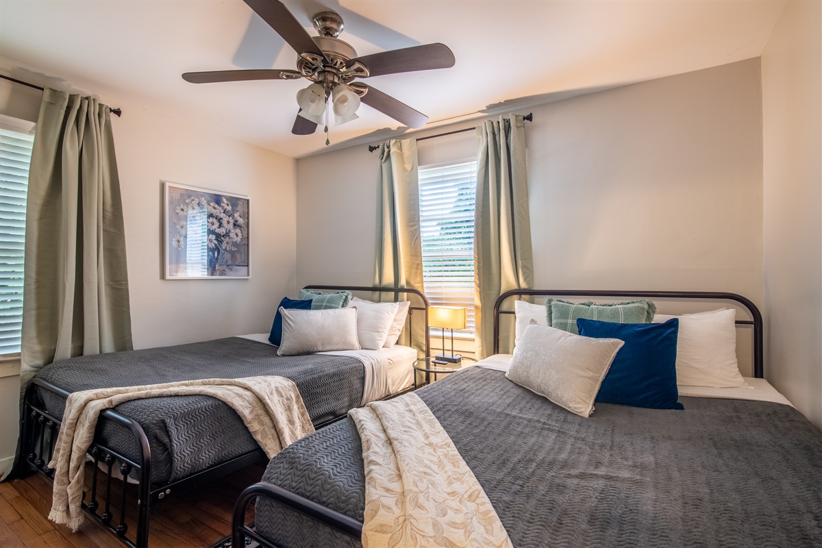 Double twin bedroom ideal for friends or kids, featuring blackout curtains, ceiling fan, and soft bedding.