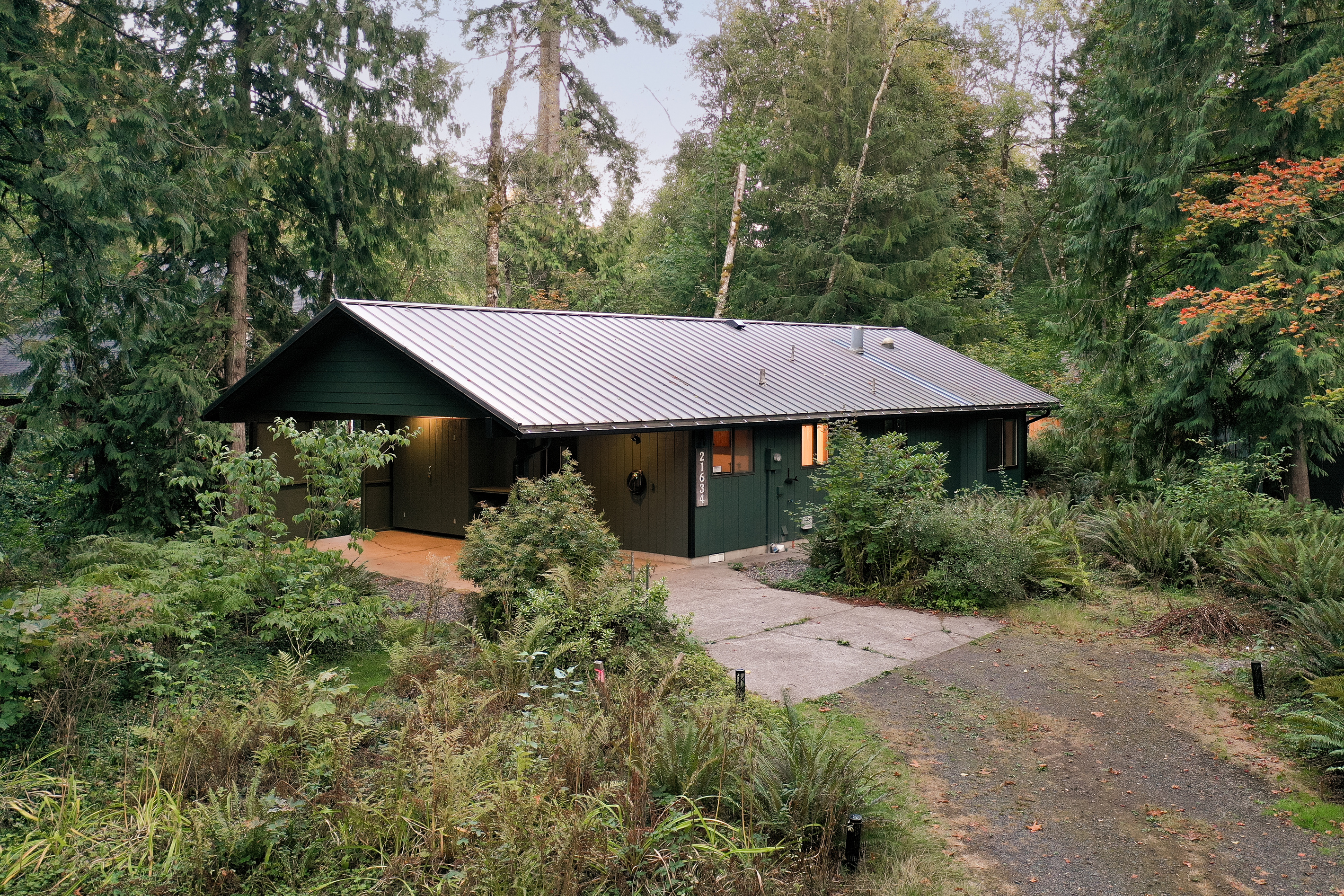 A classic green cabin tucked into the woods, glowing warm as evening settles in.