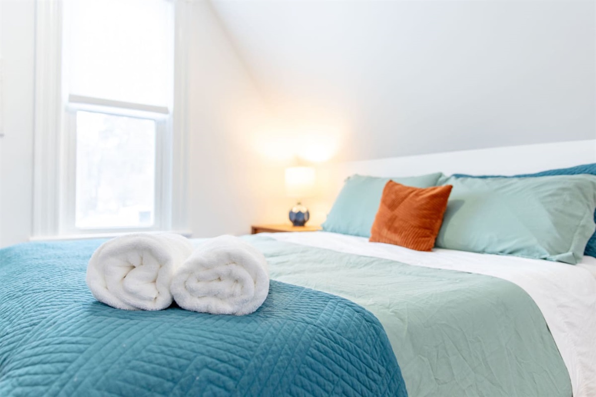 A neatly arranged bed with soft pillows, accompanied by neatly folded towels, creating a clean and inviting atmosphere for a restful stay.