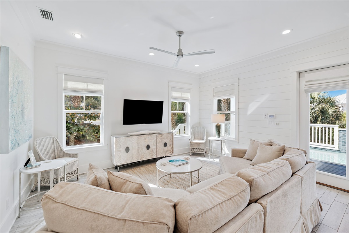 Spacious, open-concept living area filled with natural light, featuring ample seating and seamless flow to the kitchen and outdoor pool area.