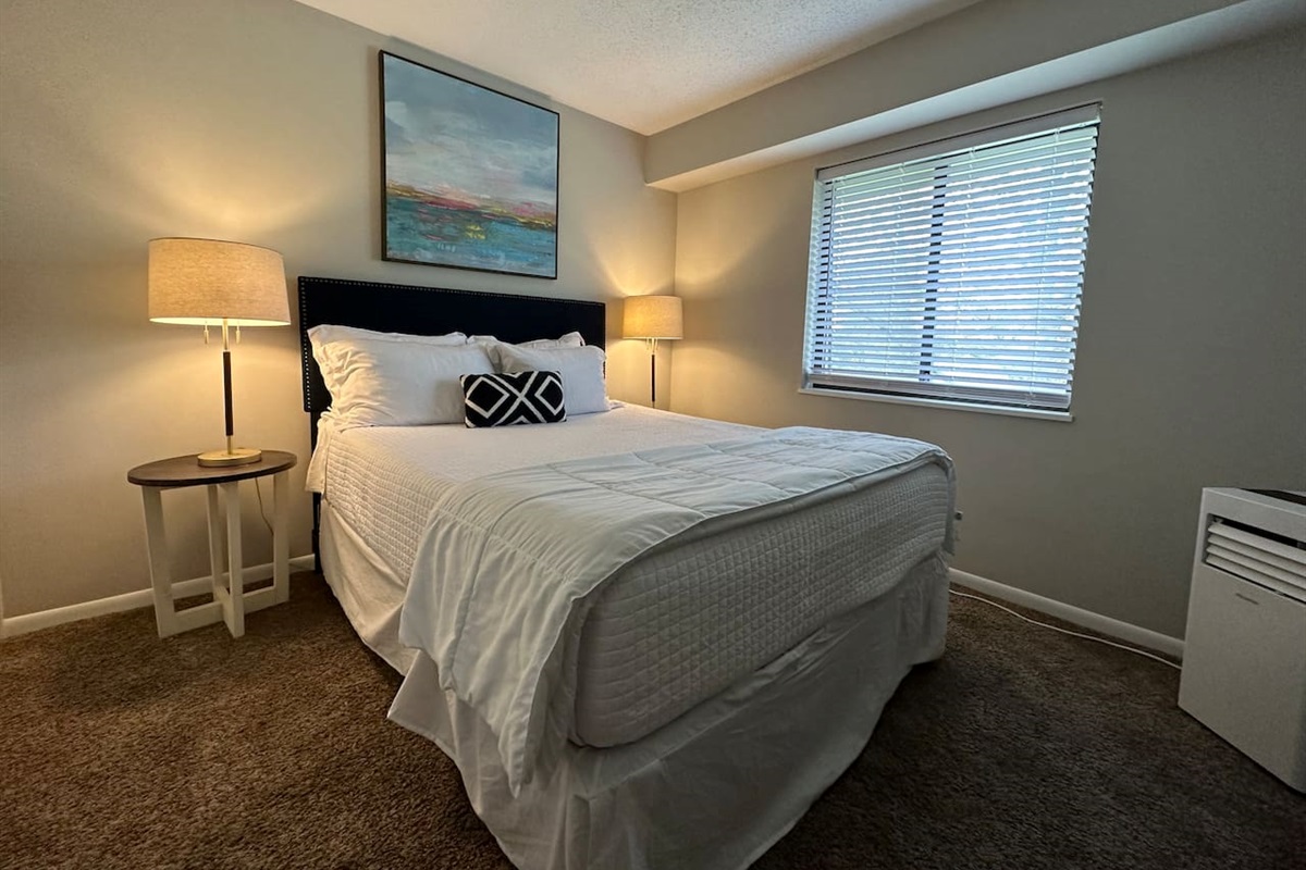 Relax in a cozy queen bed with plush bedding, soft lighting, and peaceful natural light.