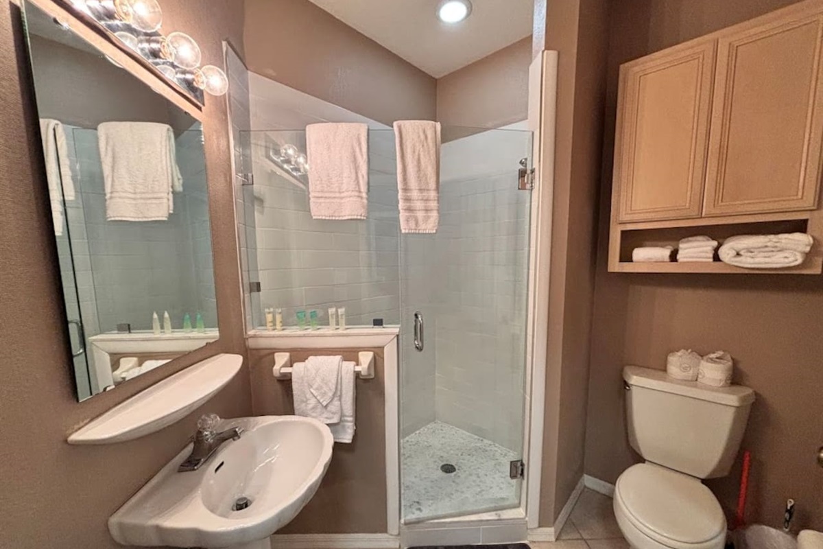 Bathroom featuring a pedestal sink, bright vanity lighting, glass-enclosed shower, and clean neutral finishes.