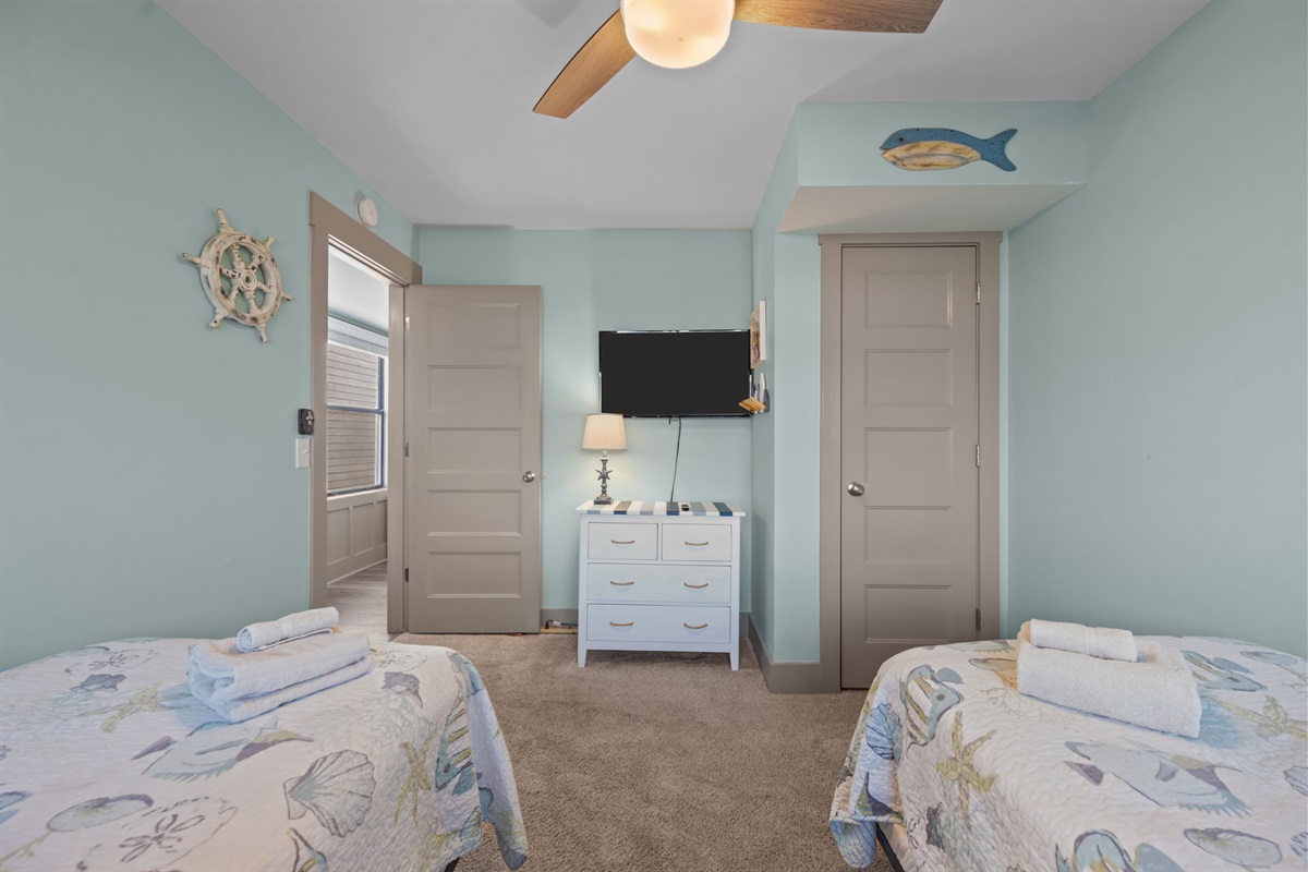 Two Twin beds with playful coastal d&eacute;cor, a wall-mounted TV, and a comfortable setup designed for kids or extra guests to unwind and feel at home