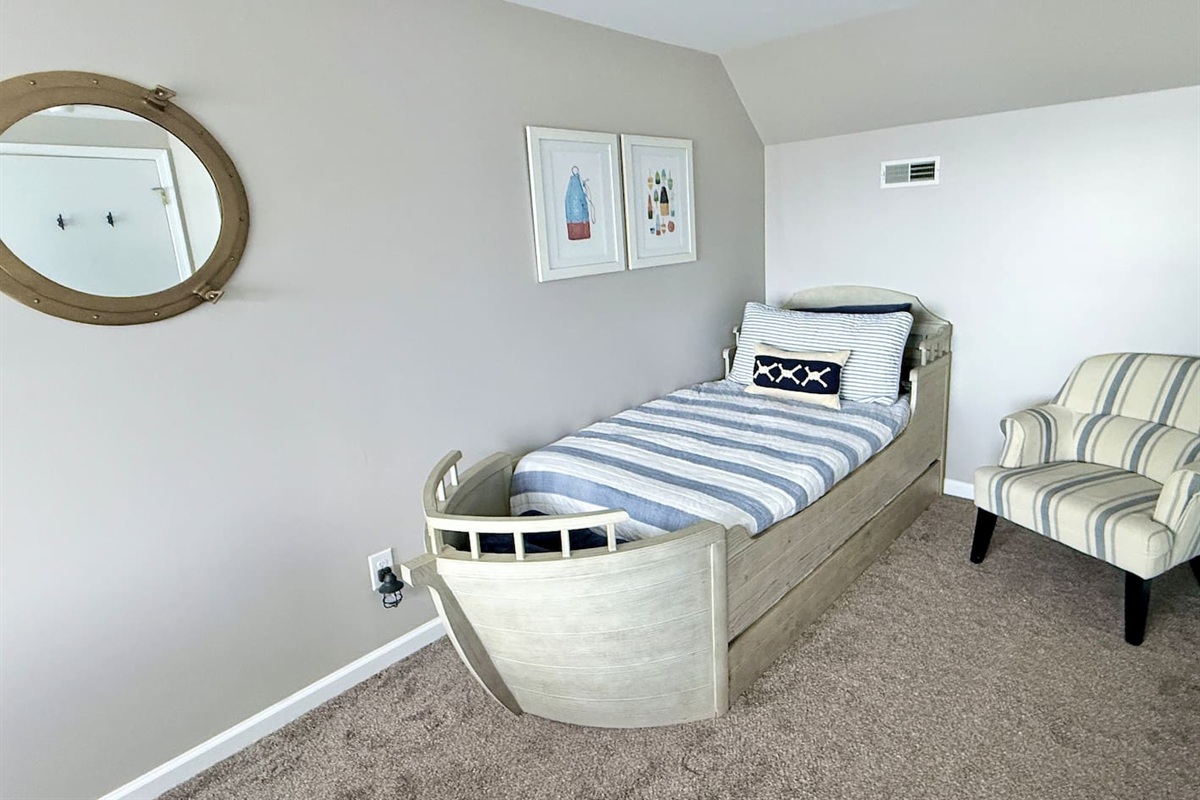 The kids will love the nautical-themed bedroom features a unique bed shaped like a boat, complemented by a round porthole-style mirror, striped accent chair, and framed coastal wall art to create a charming, sea-inspired retreat.