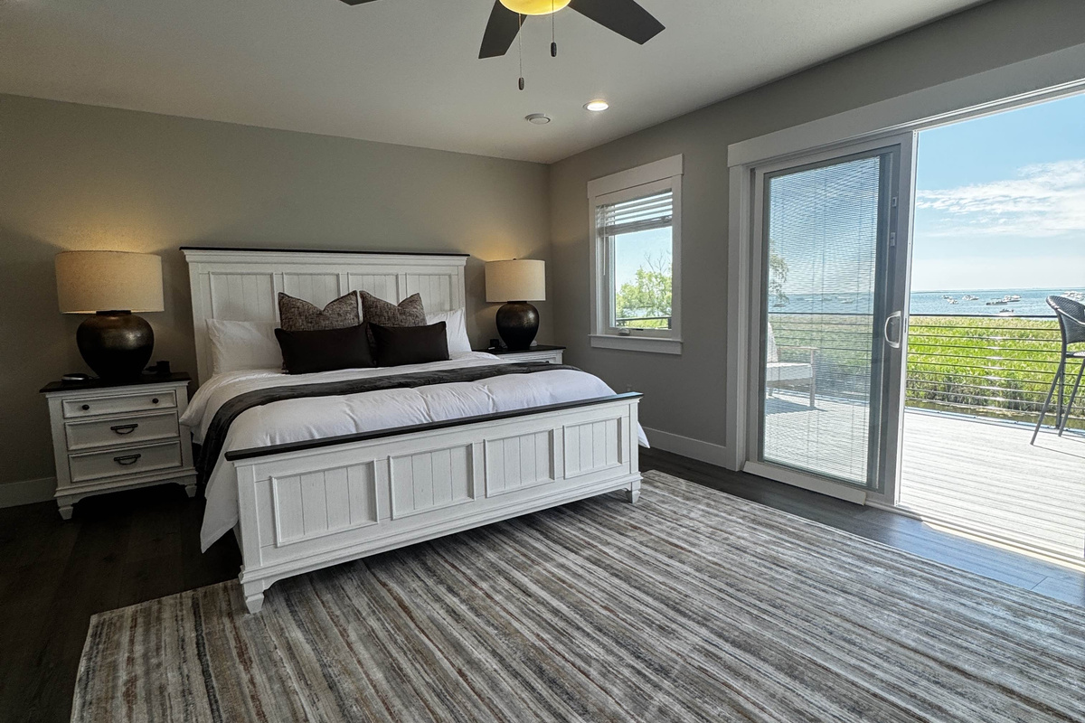 Bright and spacious bedroom with a king bed, modern furnishings, and private balcony access offering serene waterfront views—perfect for a relaxing stay.