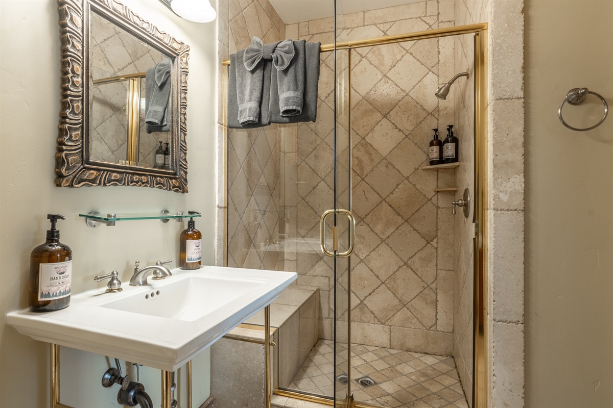 Pedestal sink, glass shelving, and spa-style finishes in the hall bath off the living area.