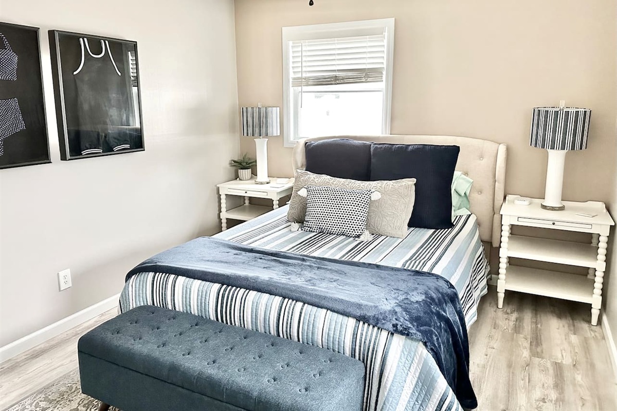 Relax in this beautifully appointed guest room, featuring a tufted headboard and a plush bed layered with navy and white striped linens. Two matching bedside tables with striped lamps and a comfortable storage bench complete this tranquil coastal escape.
