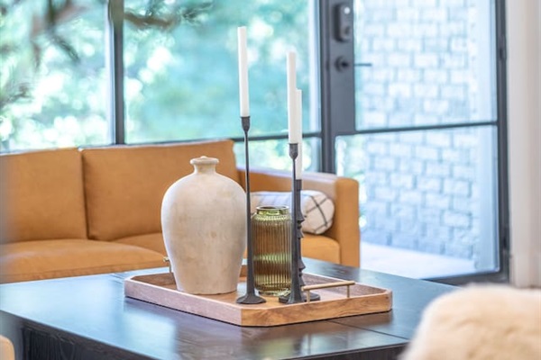 Living room detail featuring a styled coffee table with curated décor, warm wood tones, and natural light from oversized windows.