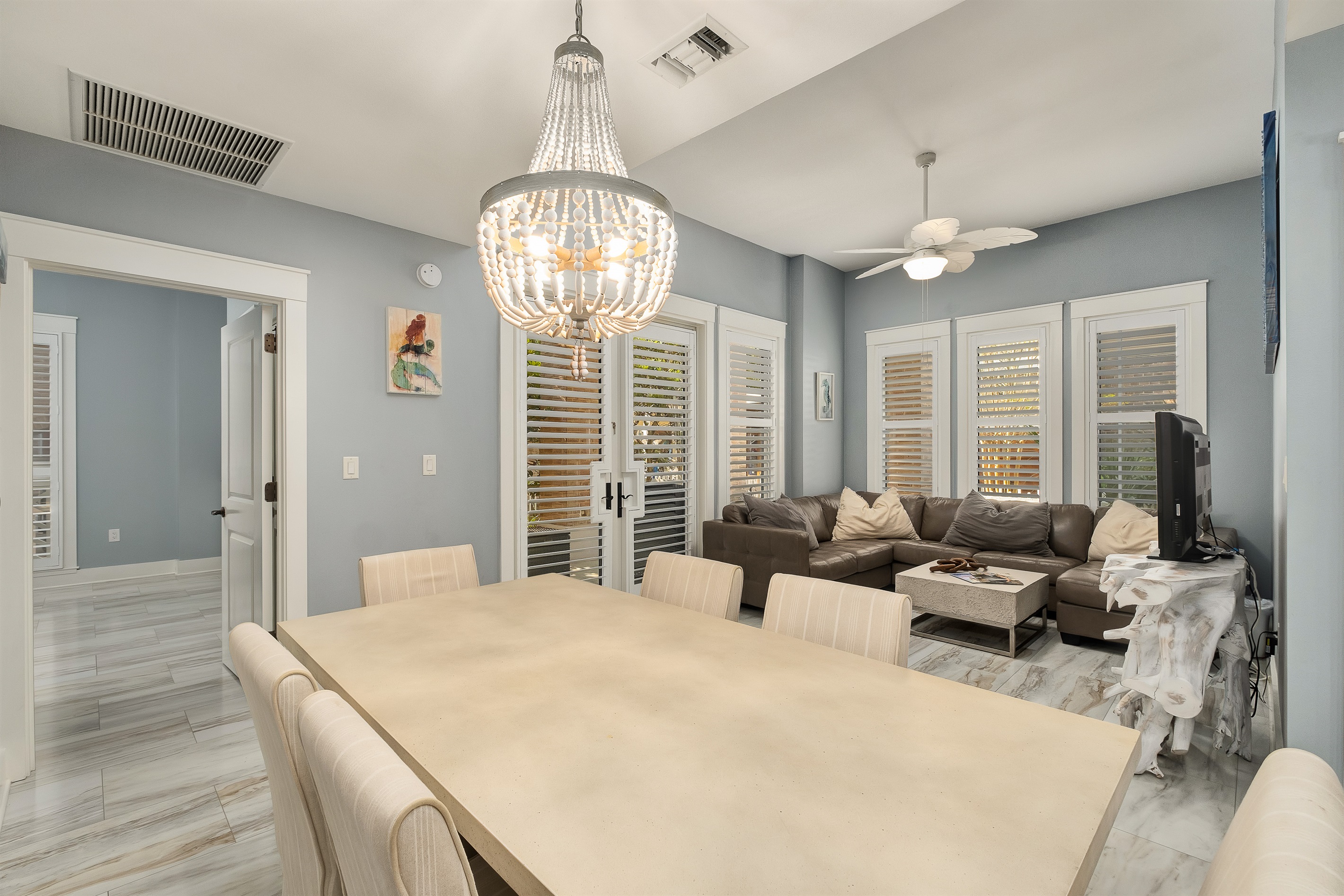 Relax and unwind in the cozy living room, complete with a comfortable sectional and large windows for plenty of natural light. The stylish dining area sits beneath a statement chandelier, creating a perfect atmosphere for meals or gatherings.