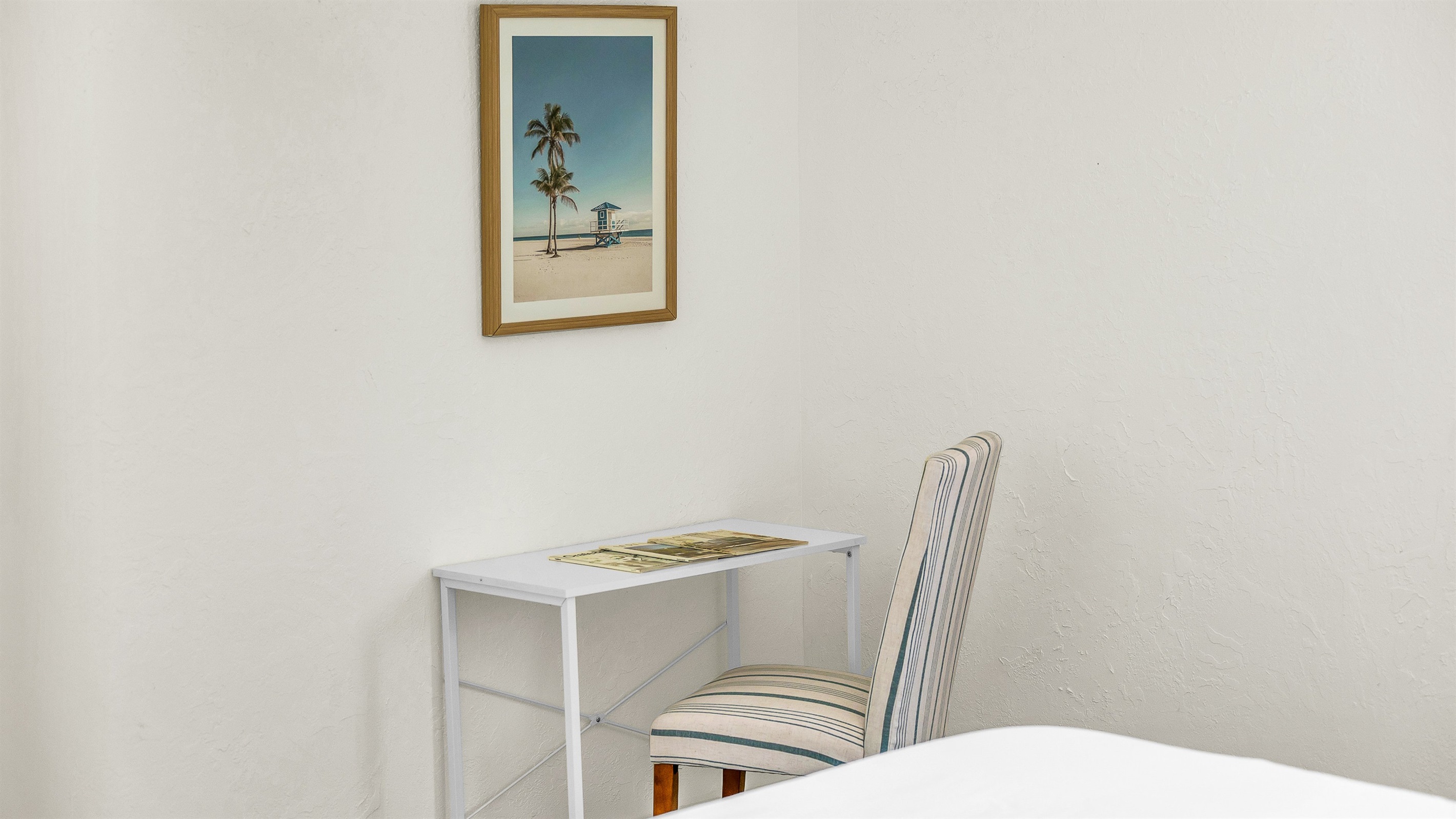 A cozy workspace tucked into Bedroom 3 offers the perfect spot to catch up on emails or plan your next beach day, featuring a minimalist desk set up and calming coastal decor