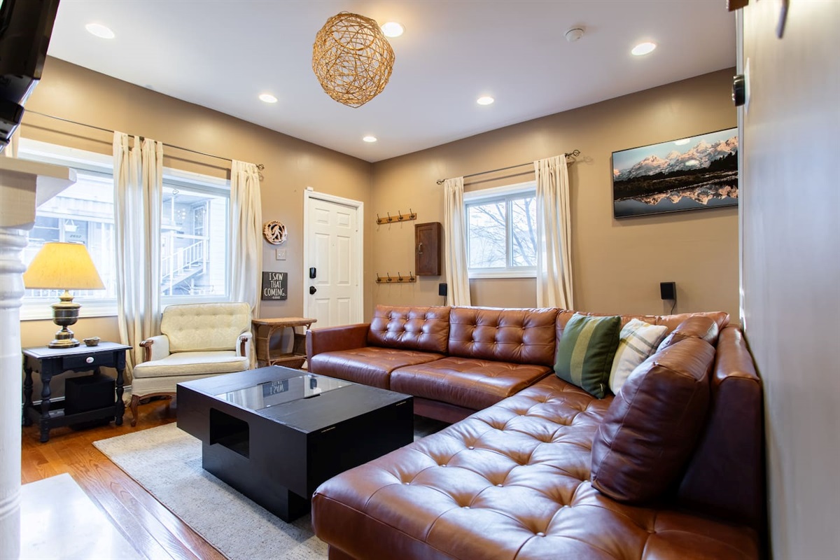 Bright and stylish living room with a spacious leather sectional, cozy accent seating, and warm lighting—perfect for relaxing after a long day