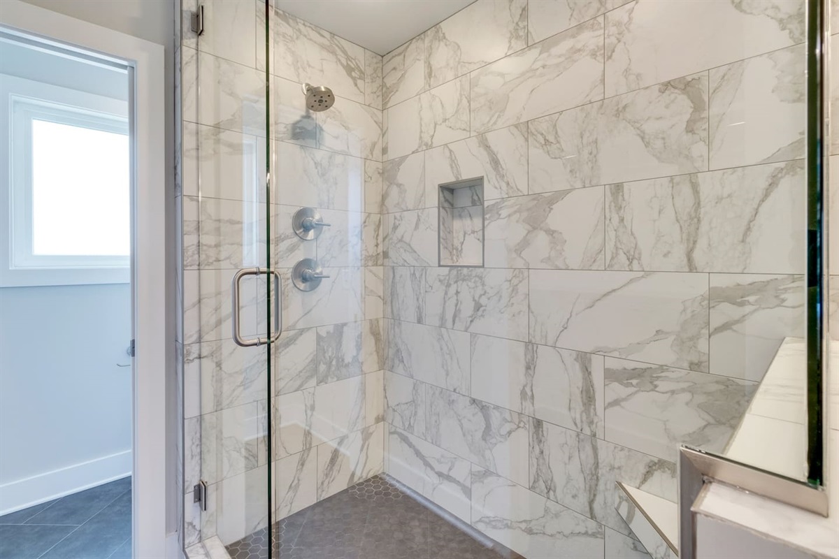 - Frameless glass doors reveal stunning marble tile with soft gray veining throughout - Built in niche for convenience and multiple spray heads for a refreshing experience - Soft lighting and stone style flooring create a calming, upscale shower retreat
