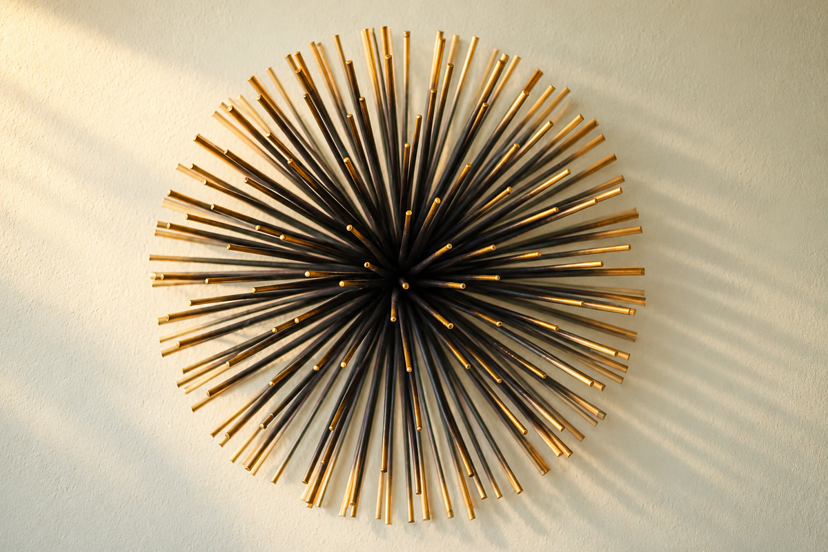 A sculptural sunburst wall piece brings a distinctive mid-century accent to the apartment. Black and gold-toned rods catch the warm light and cast delicate shadows, highlighting the thoughtful decorative details throughout the home.