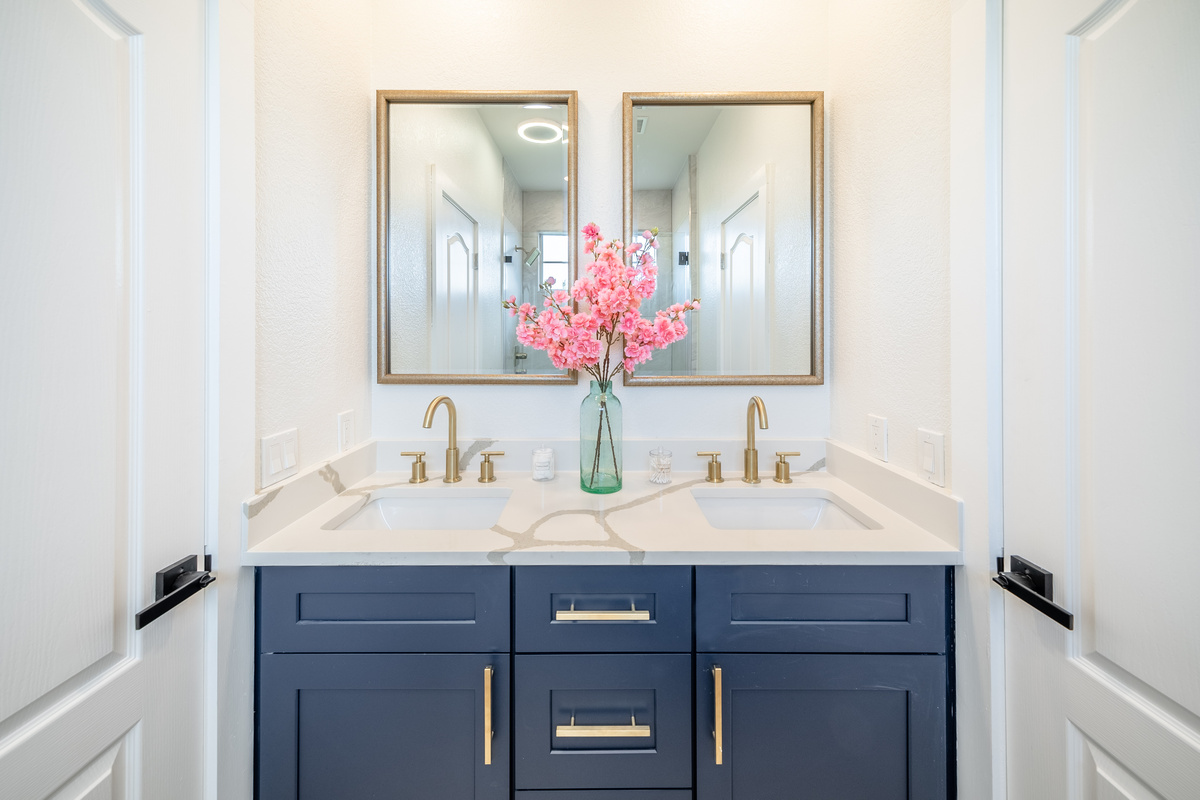 Dual gold-framed mirrors and navy cabinetry create an elegant en-suite bathroom.