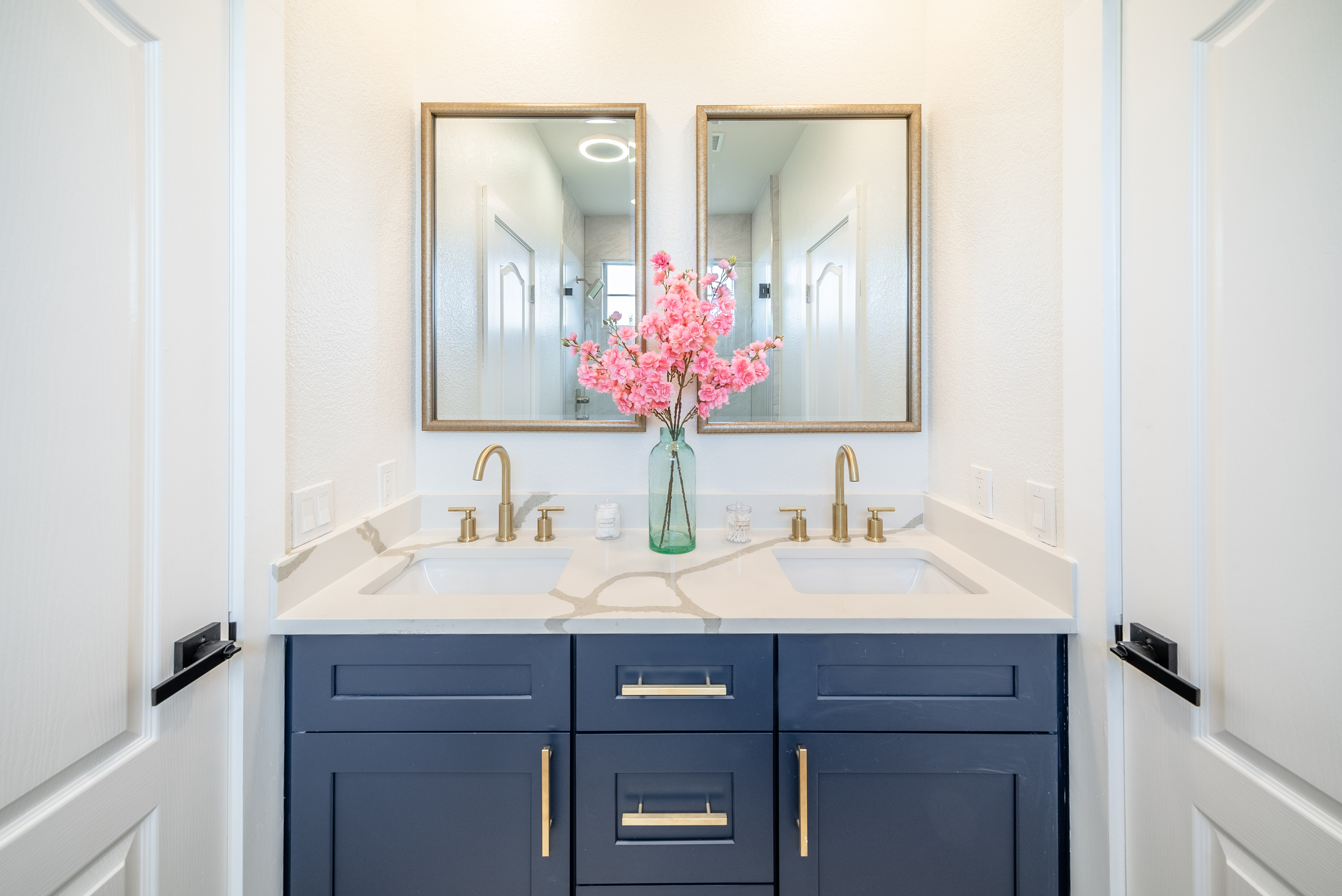 Dual gold-framed mirrors and navy cabinetry create an elegant en-suite bathroom.