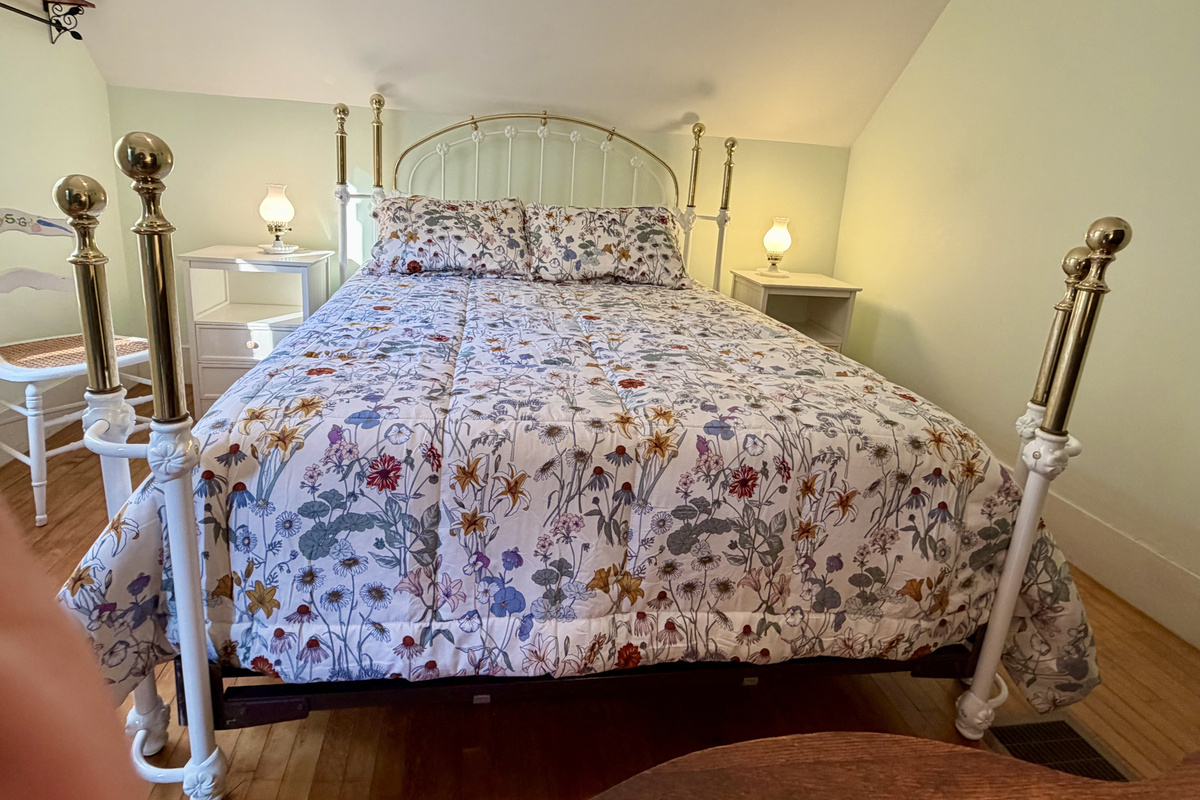 A closer look at the primary bedroom’s stunning heirloom-style brass and iron bed frame. Paired with charming floral linens, this ornate centerpiece highlights the authentic, historic character woven throughout the entire cottage.