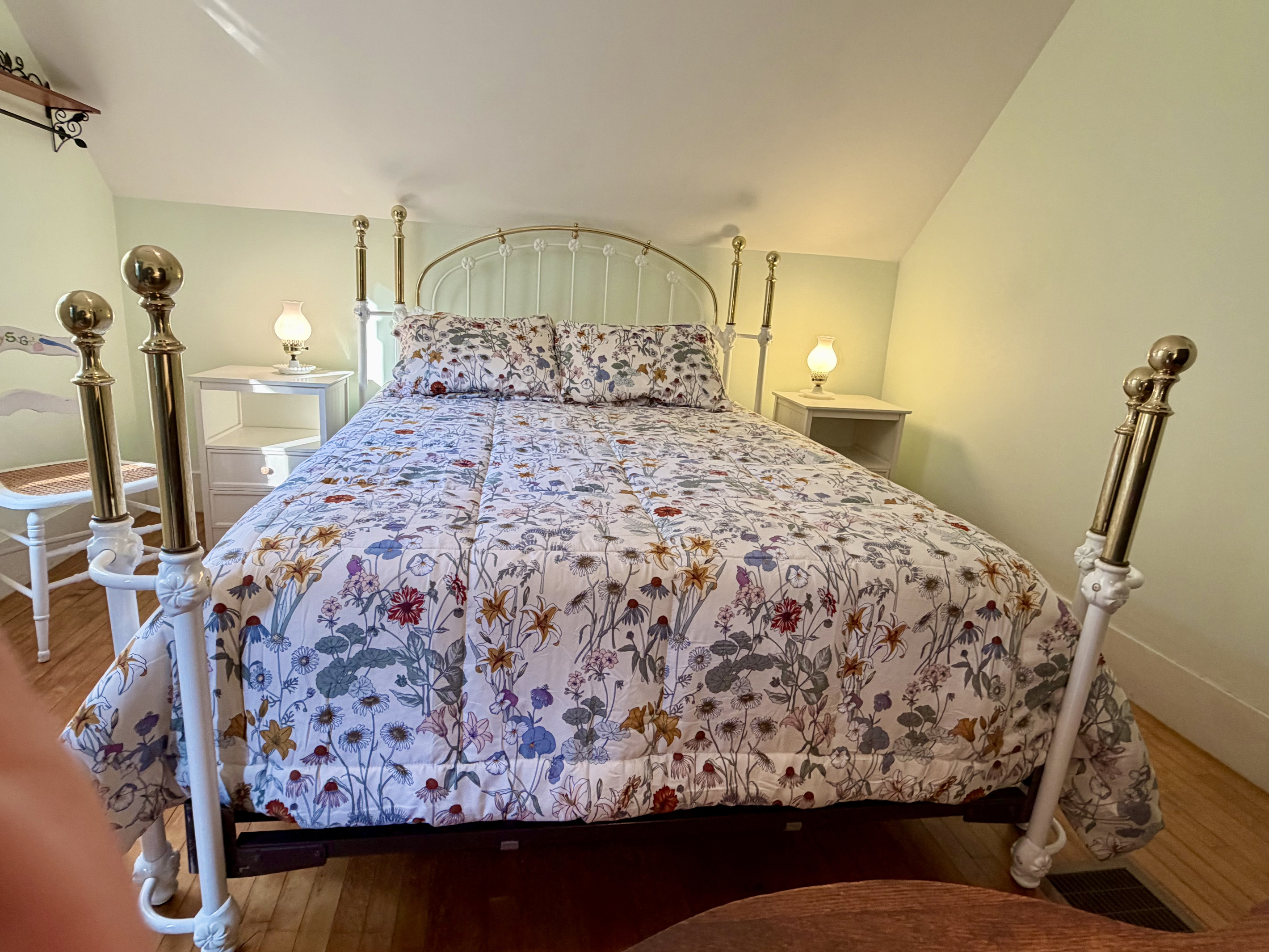 A closer look at the primary bedroom’s stunning heirloom-style brass and iron bed frame. Paired with charming floral linens, this ornate centerpiece highlights the authentic, historic character woven throughout the entire cottage.