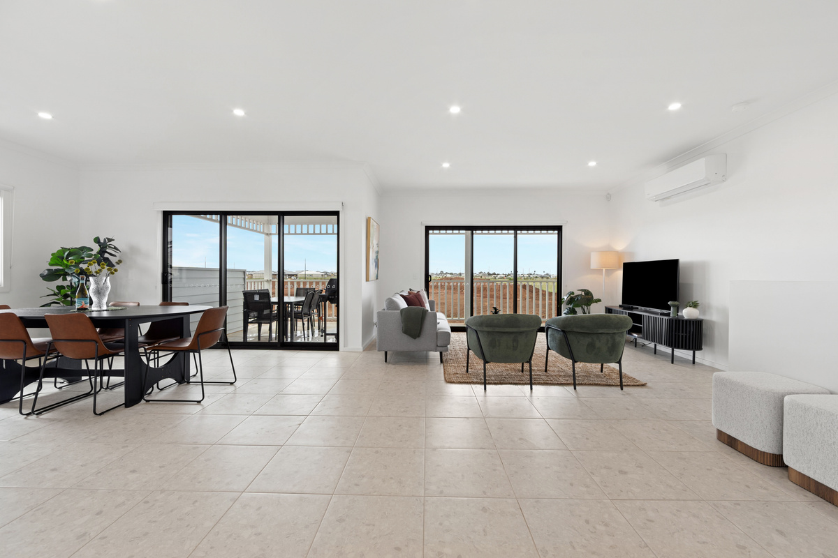 Open-plan lounge and dining space with a TV, sofa and armchairs, split-system air conditioning and sliding doors to the balcony.
