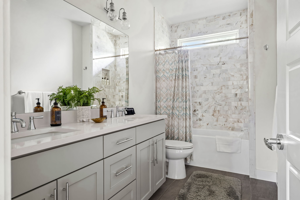 Modern guest bathroom featuring a marble-tiled accent wall, sleek vanity, and curtained tub/shower combo — bright and beautifully appointed.