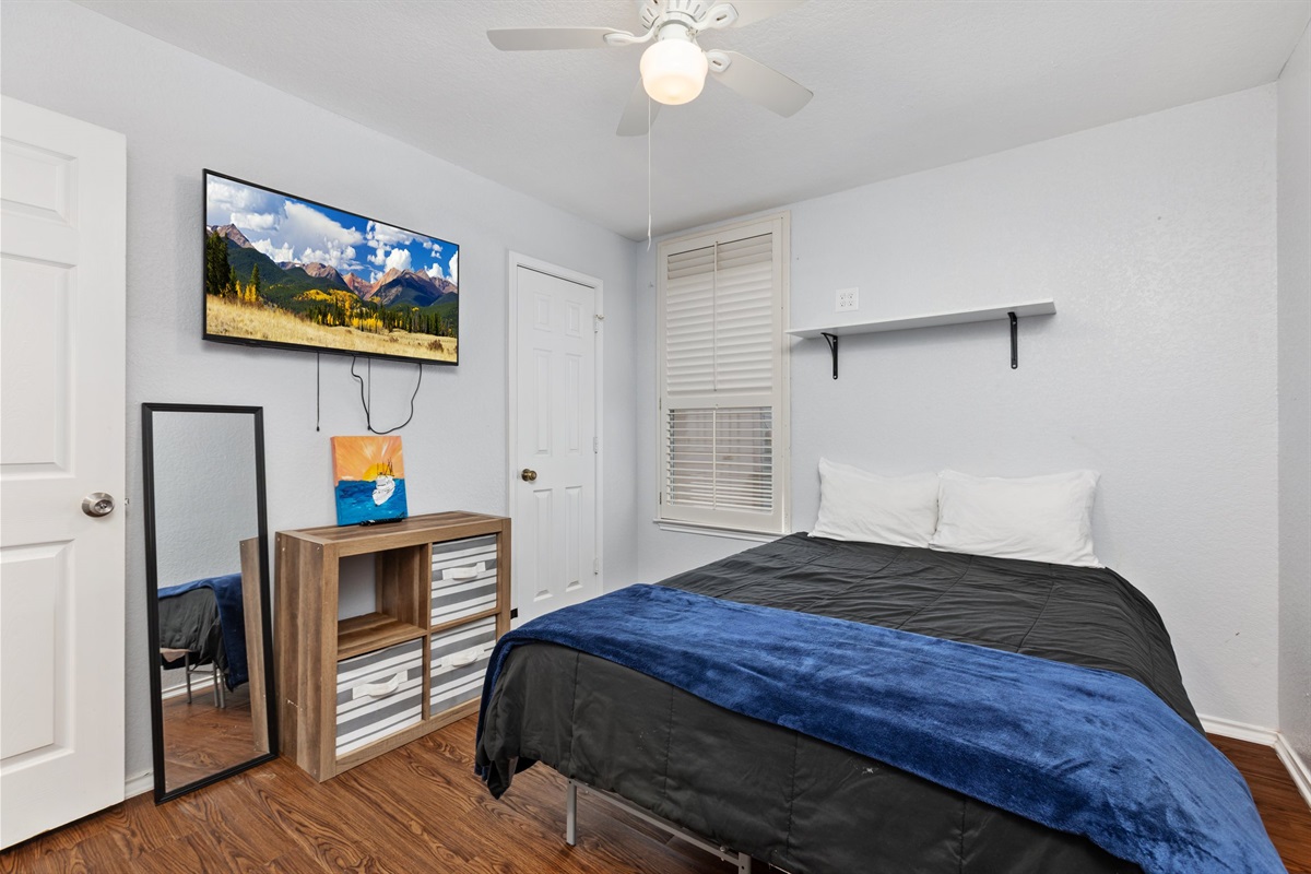 Bedroom with wall-mounted Smart TV, streaming access, dresser for clothing storage, ceiling fan, and hotel-quality bedding. Extra pillows and blankets included. Current decorative blankets, bedding, and wall art are not shown in these photos.