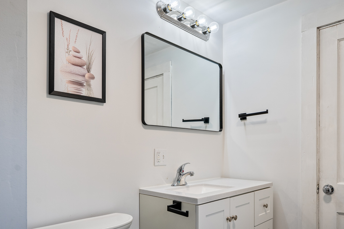 This interior view highlights our second floor bathroom vanity setup and white sink cabinet. Featuring modern black hardware, an extra-wide wall mirror, and bright vanity lighting, this layout delivers great functional utility for your Maine stay.
