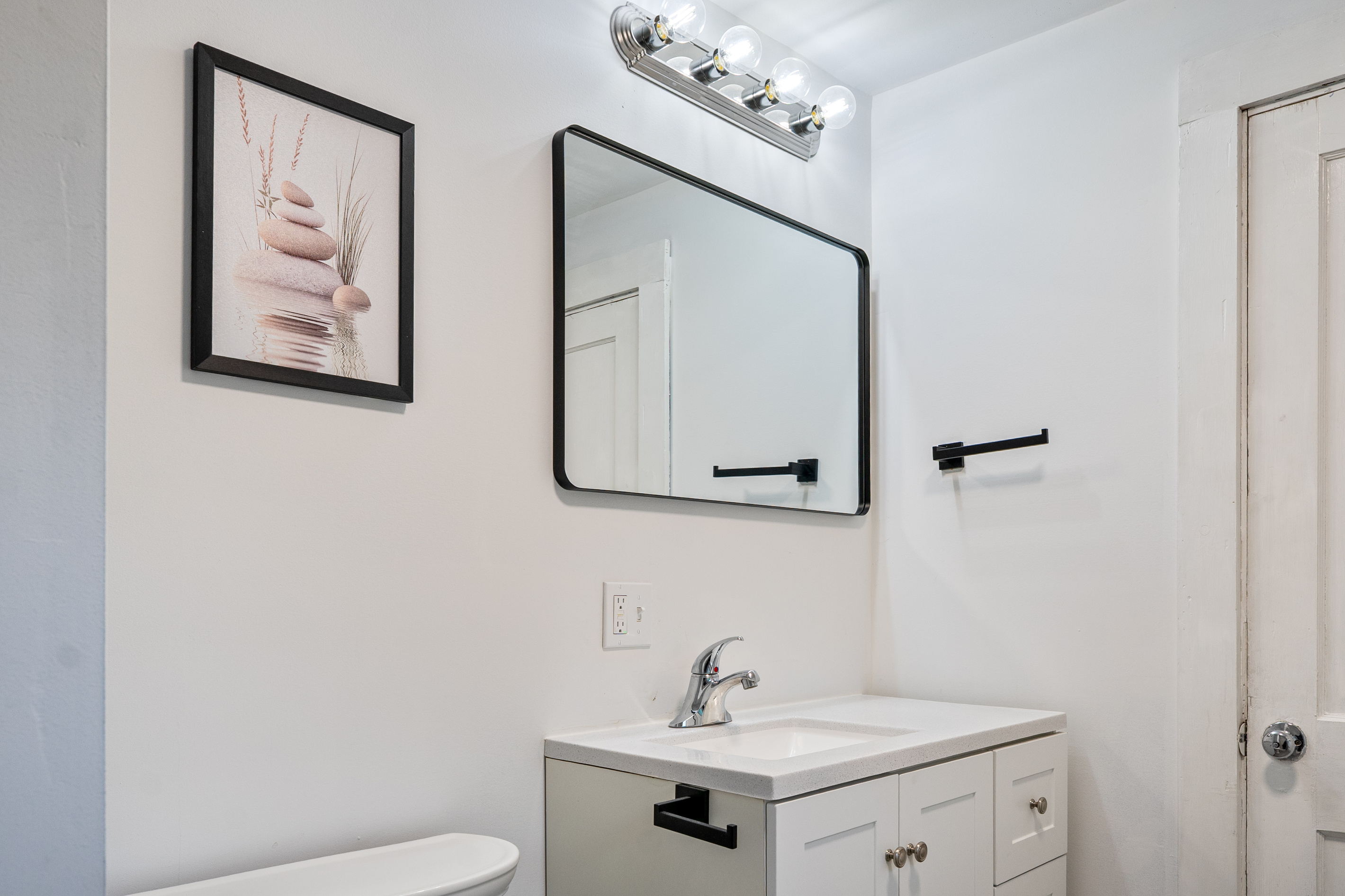 This interior view highlights our second floor bathroom vanity setup and white sink cabinet. Featuring modern black hardware, an extra-wide wall mirror, and bright vanity lighting, this layout delivers great functional utility for your Maine stay.