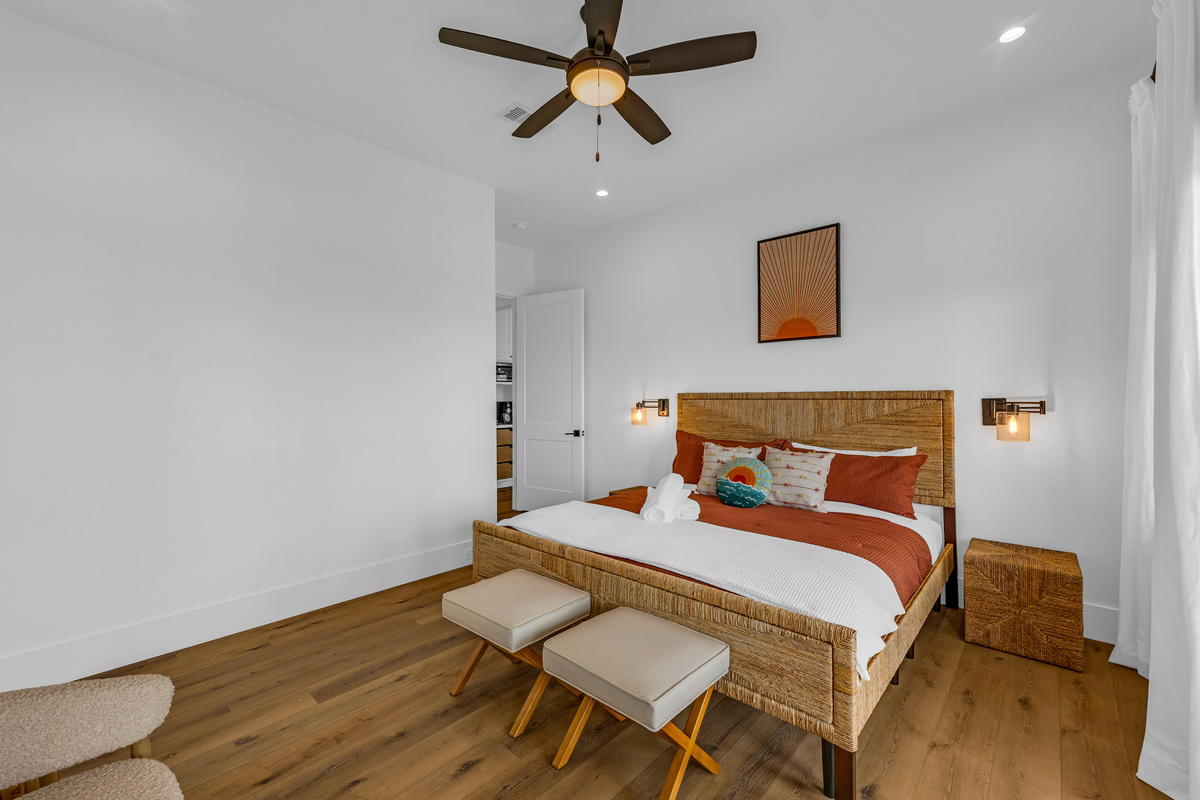 Cair Paravel: Sun-washed coral and rust tones warm this king bedroom, where a woven headboard and private deck access invite guests to wake up to the Gulf.