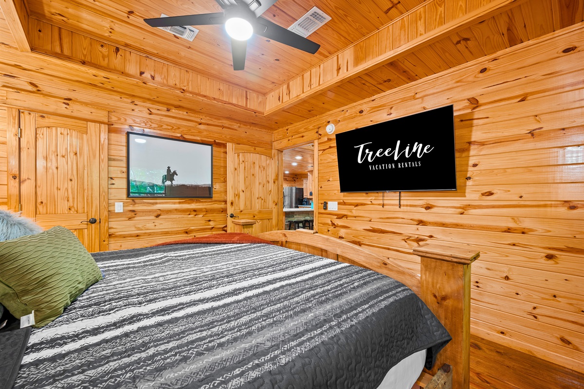 Primary bedroom includes a mounted flat-screen TV, warm wood paneling, and thoughtful rustic touches.