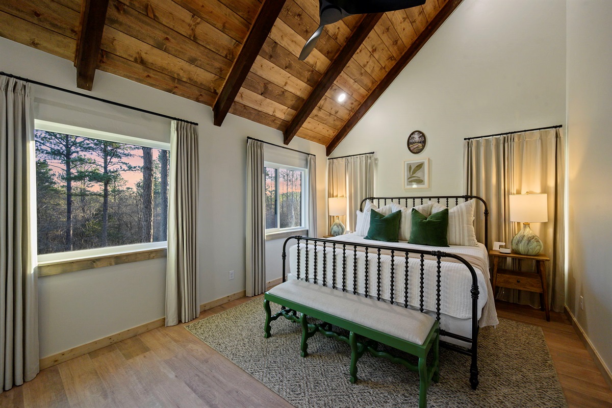 Vaulted king retreat with large windows and peaceful wooded backdrop.